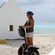Two women ride Segways on a beach with huts